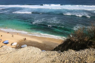 Pandawa Sahili 'nde geniş bir açı, Bali' de kumlu sahilde şemsiyeler, okyanusta güçlü dalgalar ve mavi bir gökyüzü.