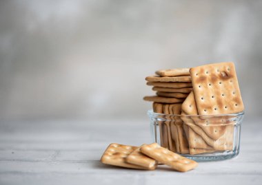 Kare buğday krakerleri beyaz bir masada cam bir kase içinde