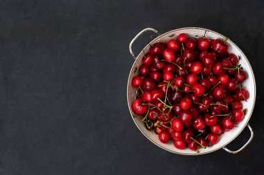 Siyah arka planda beyaz kevgir içinde olgun kırmızı kirazlar.