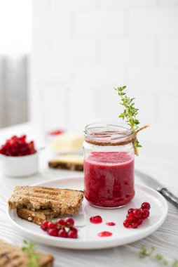 Frenk üzümü reçelli kahvaltı, beyaz tabakta çavdar ekmeği ve tereyağı.