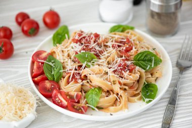 beyaz tabakta domates soslu fettuccine, parmesan ve fesleğen.