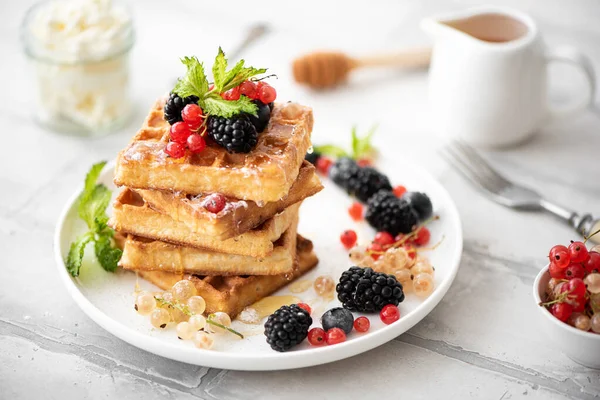 homemade waffles with berries, powdered sugar, drizzled with honey on white plate