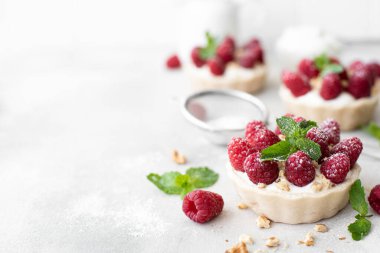 Maskopon peynirli tartlar, taze ahududu ve fındıklar, beyaz masada.