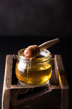 Siyah arka planda tahta bir kutuda küçük bir bal kavanozu.