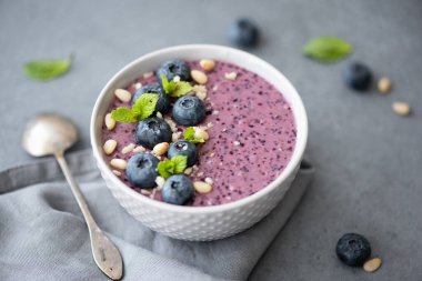 Nane ve çam fıstıklı gri bir kasede yaban mersinli smoothie.