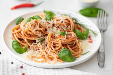 Beyaz tabakta fesleğenli ve parmesanlı spagetti bolonez.