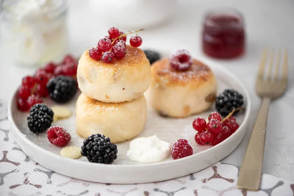 cottage cheese pancakes with berries and sour cream on a grey plate