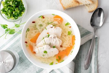 Erişteli tavuk çorbası ve beyaz tabakta otlar.