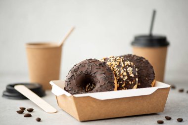 El işi kutusunda jöleli çikolatalı çörekler ve beyaz bir masada fincanlarda sade kahve.