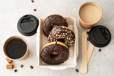 El işi kutusunda jöleli çikolatalı çörekler ve beyaz bir masada fincanlarda sade kahve.