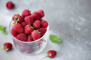 Gri bir masada cam bir kasede olgun büyük ahududular.
