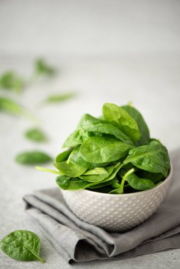 Beyaz bir masada gri bir kasede taze ıspanak yaprakları.