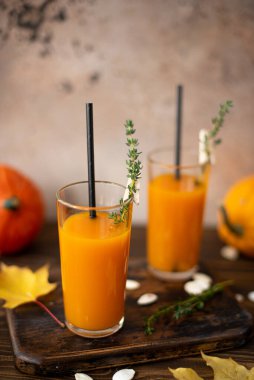 Tahta bir masanın üzerinde uzun gözlüklü kekik ile taze sıkılmış balkabağı suyu.