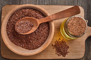 Tahta bir masada keten tohumu ve tahta bir kaşık. Bir şişe yağlı tahta kase. Sağlıklı yiyecek ve içecek konsepti. Uzayı kopyala Kapat.