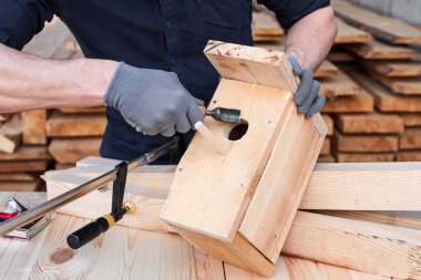 Zanaatkar ahşap bir kuş evi yapıyor, aletler, ekipmanlar ve ahşap kalaslarla, eller kapalı.