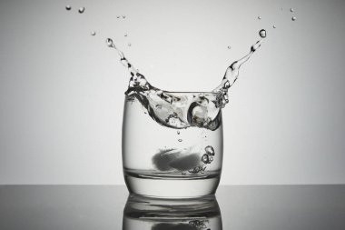 Su damlaları, damlalar ve hava kabarcıkları olan bir bardak suya buz düşer..