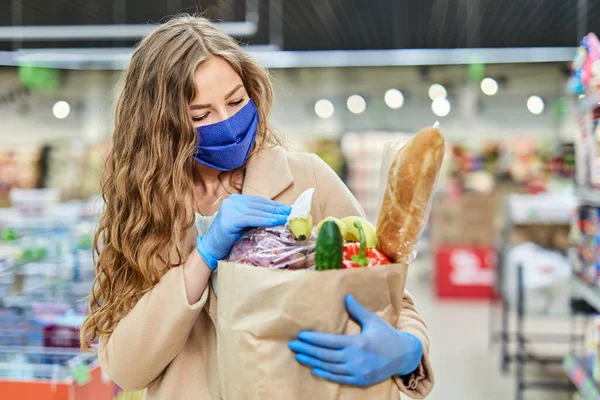 Bakkal paketleri silen, eldiven takan, mendil kullanan bir kadın. Covid-19 salgını sırasında alışveriş..