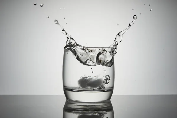 Jég esik egy pohár víz fröccsenés, csepp és légbuborékok. — Stock Fotó