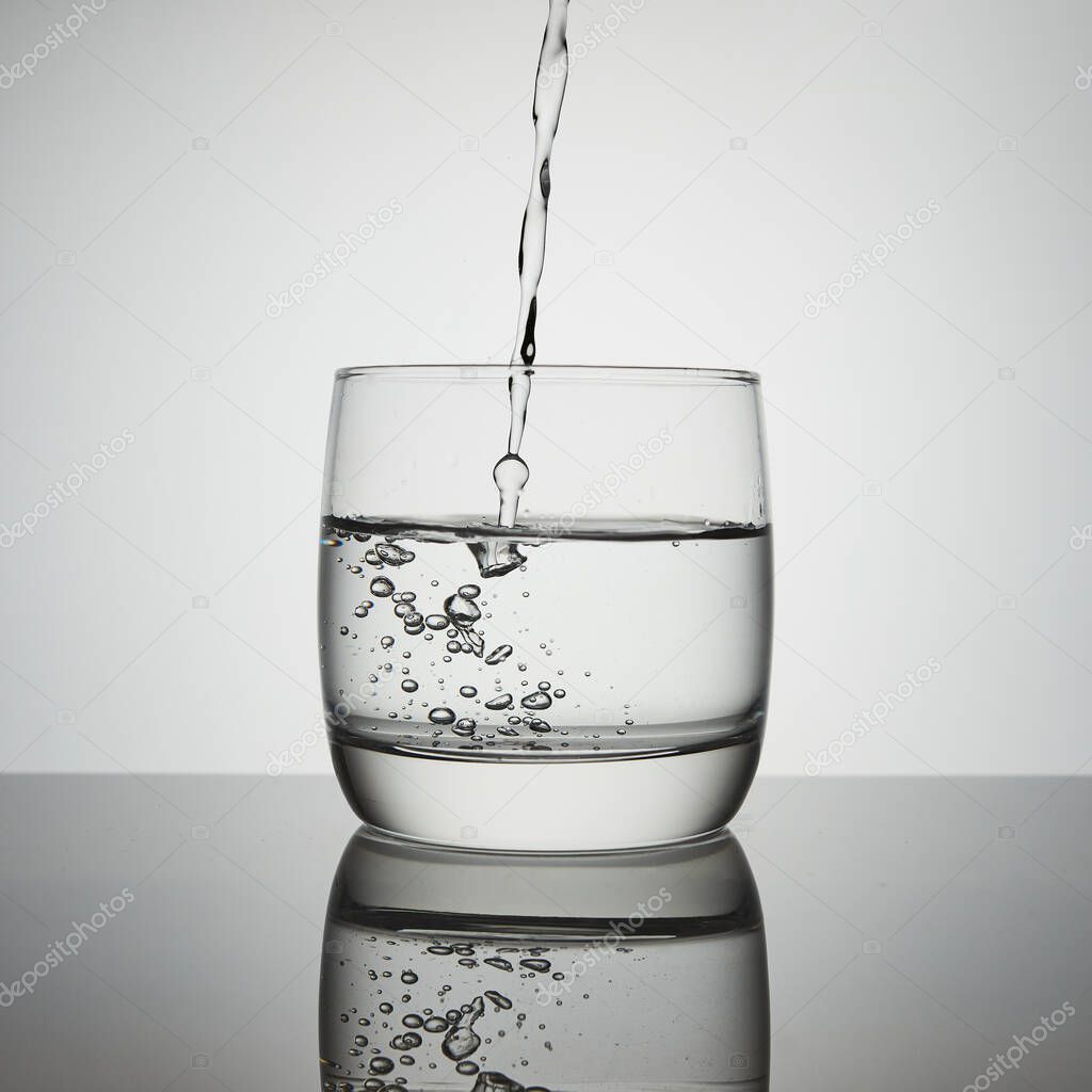 Water pouring into glass. Transparent Water jet falling into a glass. Splashes, drops, air bubbles from a aqua stream.