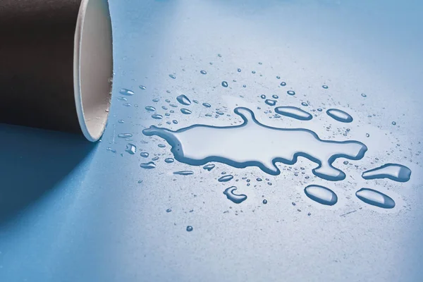 Taza de papel oscuro con gotas abstractas de agua derramada sobre fondo azul. Bebida de alcohol derramado concepto taza. — Foto de Stock