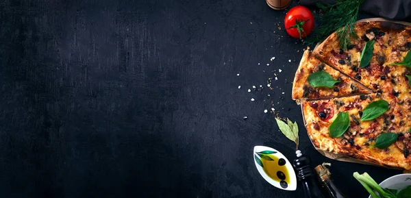 Italian pizza and pizza cooking ingredients on dark background. Tomatoes, olives oil, herbs and spices.
