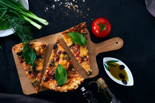 Italian pizza and pizza cooking ingredients on dark background. Tomatoes, olives oil, herbs and spices.