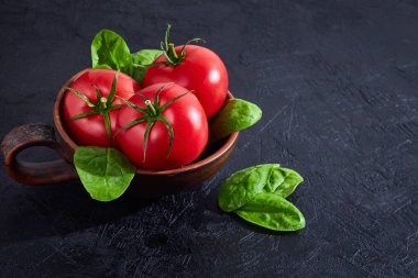 Siyah taş arka planda ıspanaklı taze üzüm domatesleri. Vejetaryen sebze diyeti. Bitki, domates, aşçılık konsepti.