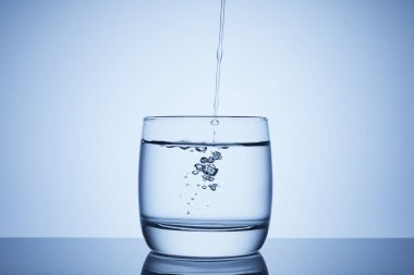 Su cama dökülüyor. Şeffaf su jeti bardağa düşüyor. Su birikintisinden gelen su damlaları, hava kabarcıkları. Kapat..