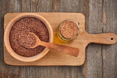 Tahta bir masada keten tohumu ve tahta bir kaşık. Bir şişe yağlı tahta kase. Sağlıklı yiyecek ve içecek konsepti. Uzayı kopyala Kapat.