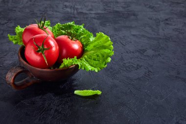 Salata salatalı taze üzüm domatesleri siyah taş arka planda yapraklar. Vejetaryen sebze diyeti. Bitki, domates, aşçılık konsepti.