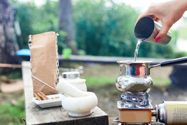 Sıcak bir şeyler içelim. Doğada baharatlı kahve pişirme süreci. Arka plan - kamp ve orman.