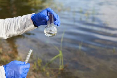 Su Saflığı Testi. Kimyasal bir matara ya da su ile test tüpü tutarak. Arka planda göl ya da nehir.