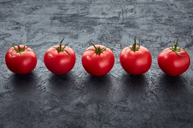 Koyu taşlı arka planda olgun kırmızı domatesler. Pişirmeye hazır taze domateslerin mutfak görüntüsü..