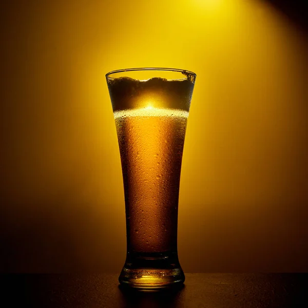 Luce artigianale fredda Birra in un bicchiere con gocce su un tavolo scuro. Pinta di birra su sfondo di colore giallo. — Foto Stock