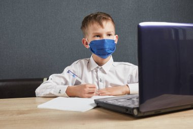 Sosyal mesafe, kendini izole etme, online eğitim konsepti. Evde online ders sırasında maskeli çocuk ödev matematiği çalışıyor..