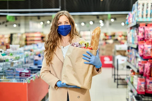 戴着医疗面罩的女信使志愿者拿着装有产品和蔬菜的纸袋 在Covid 19大流行病期间购物 — 图库照片