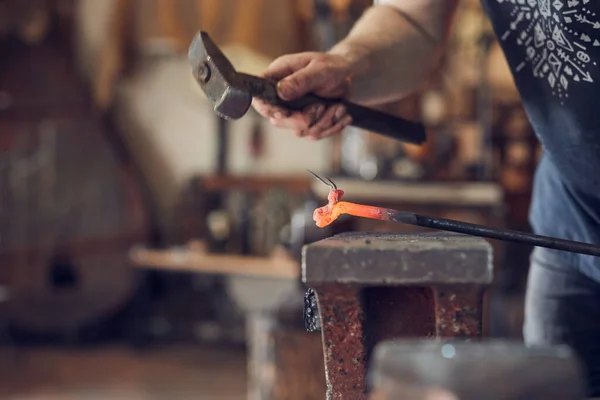 Herrero forjando manualmente sobre hierro en yunque en forja. Tratamiento del primer plano de metal fundido. — Foto de Stock
