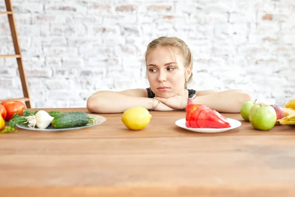 テーブルの上に寝そべっている野菜を見て悲しい女の子。食事の習慣は変わる。女は菜食が嫌い. — ストック写真