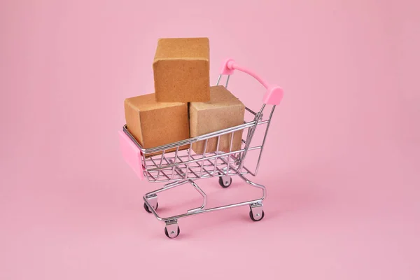 Shopping cart with package boxes on pink background. Shopping and delivering concept.