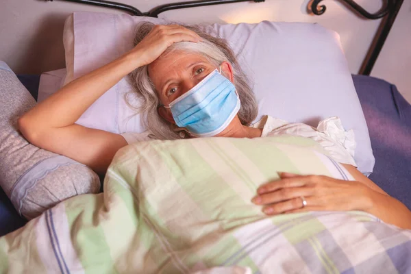Sick older woman with face mask lying on bed