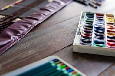 Ahşap masada renkli kalemler, fırçalar ve suluboya boyalar. Sanat ressamı aksesuarları, seçici odaklanma