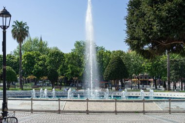 Güneşli bir günde yeşil ağaçlı şehir parkındaki çeşme..
