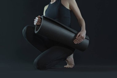 Yoga pozisyonu alan genç bir kadın. Yoga minderi ve tozluklarını esnetiyor. Siyah arka planda. kopyalama alanı. spor egzersiz egzersizi..