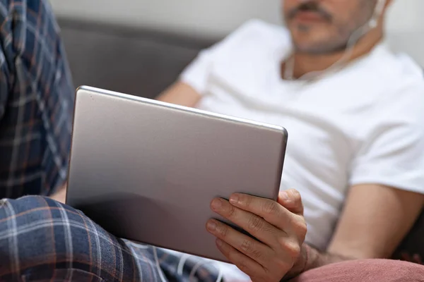 Elinde dijital tablet ve kulaklıkla evde pijamayla bekleyen bir adam. Çevrimiçi eğitim, çalışma, video çağrısı.
