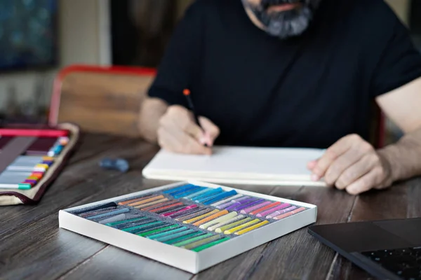 Persona aprendiendo pintura en línea con lápiz de colores pensil y pastel en hoja blanca de papel delante de la computadora portátil en la mesa de madera — Foto de Stock