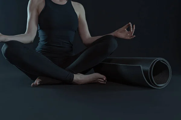 Jovem com tapete de ioga praticando ioga no fundo preto escuro. espaço de cópia — Fotografia de Stock