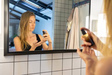 Güzel bir kadın yüz nemlendirici sürüyor, krem sürüyor, banyo aynasının önünde duruyor. güzellik tedavisi