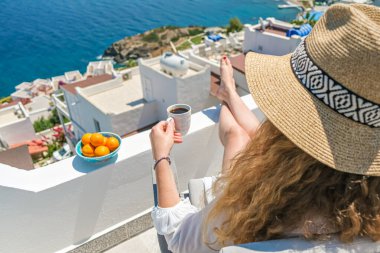 Güzel genç bayan hasır şapka ve kahve fincanı Deniz Manzaralı beyaz teras balkonunda oturuyor.