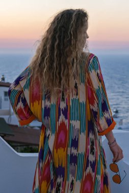 Balkonda bir kadın güzel, renkli günbatımına ve deniz dikine bakıyor.