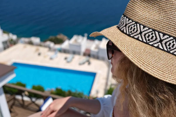 Belle jeune femme en chapeau de paille sur terrasse blanche balcon de la maison ou hôtel regardant à la piscine et vue sur la mer — Photo